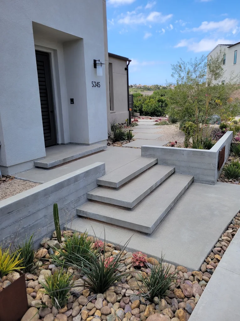 Concrete garden steps beside a low board-formed wall with boulders and succulents